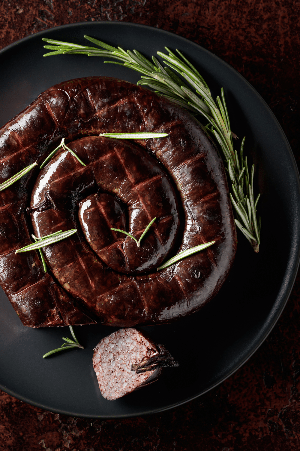 Boudin noir et romarin sur assiette noire.