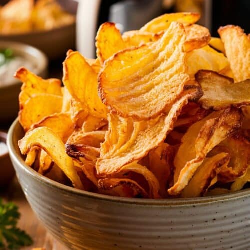 Chips dorées dans un bol devant une friteuse.