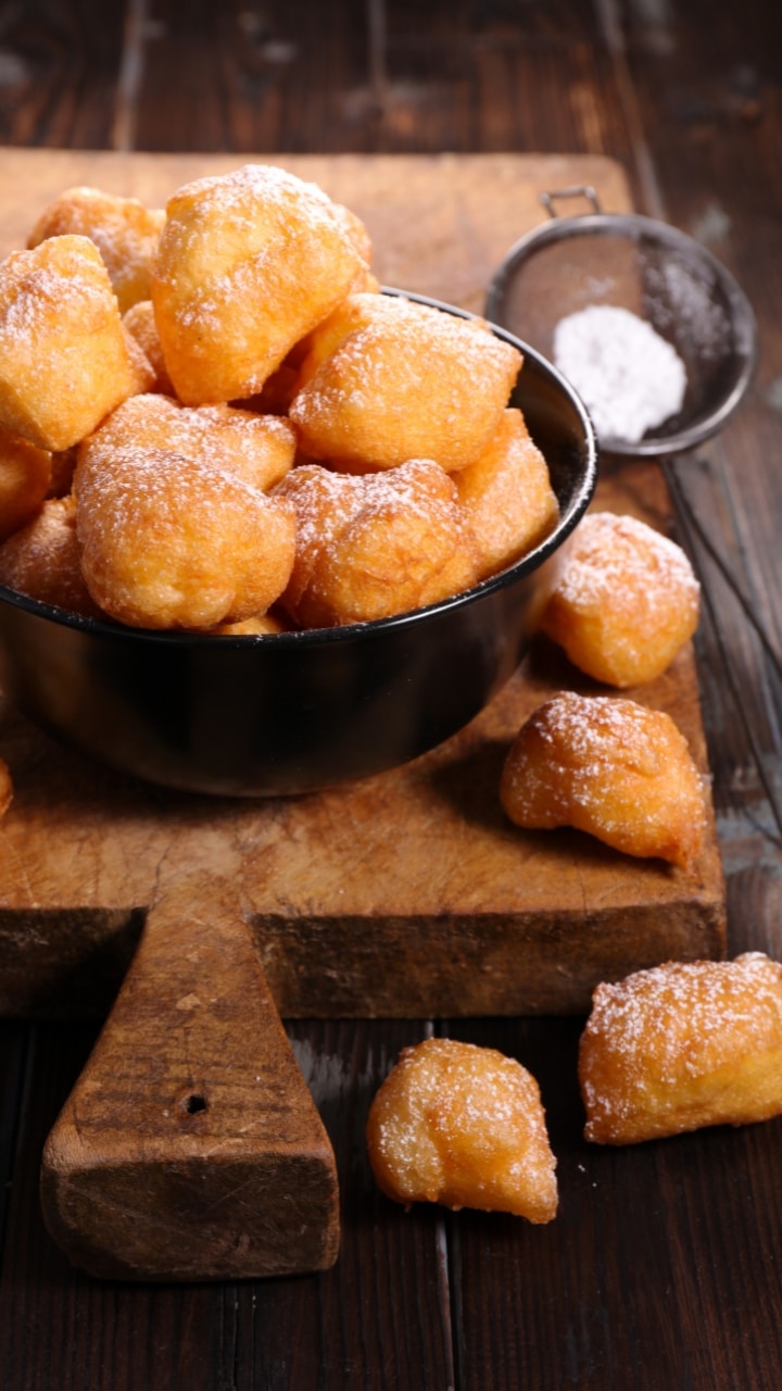 Beignets dorés avec sucre glace sur planche en bois.