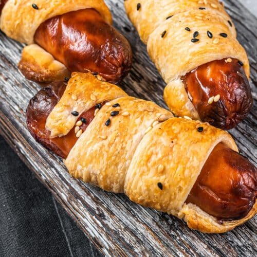 Saucisses feuilletées avec graines noires sur planche bois.