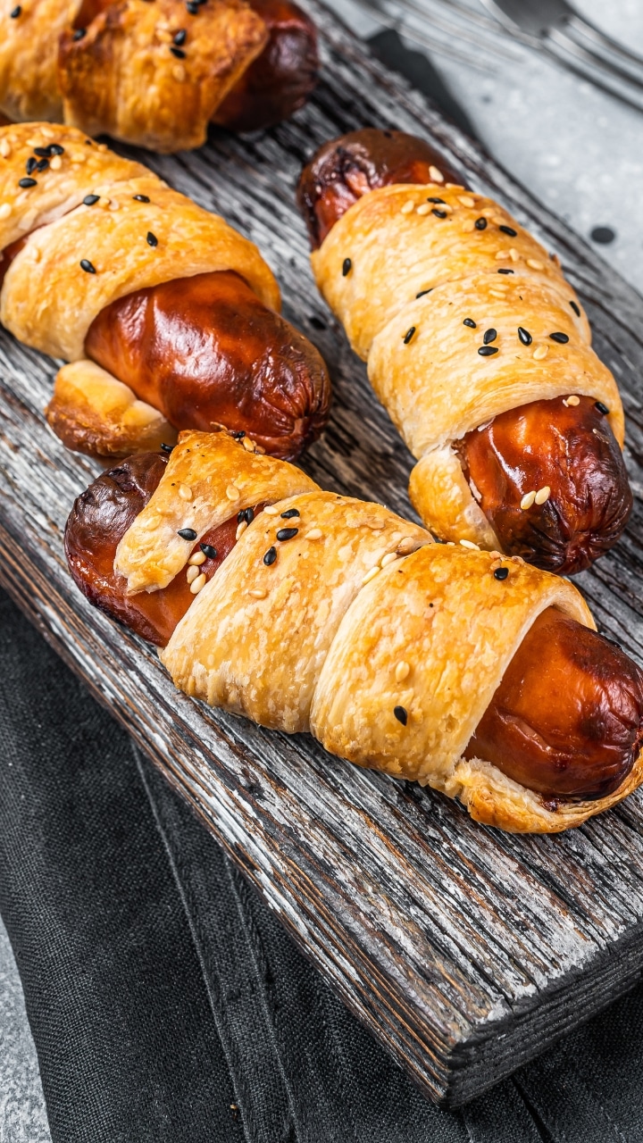 Saucisses feuilletées avec graines noires sur planche bois.