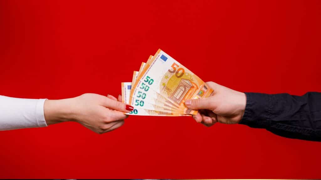 Échange de billets de banque, mains sur fond rouge.