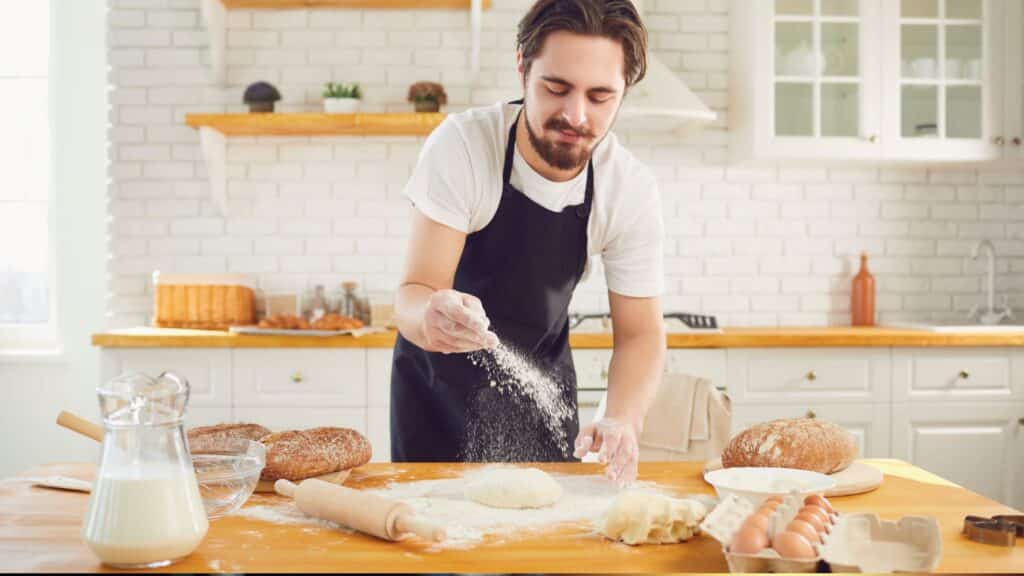 Homme préparant du pain dans une cuisine lumineuse.