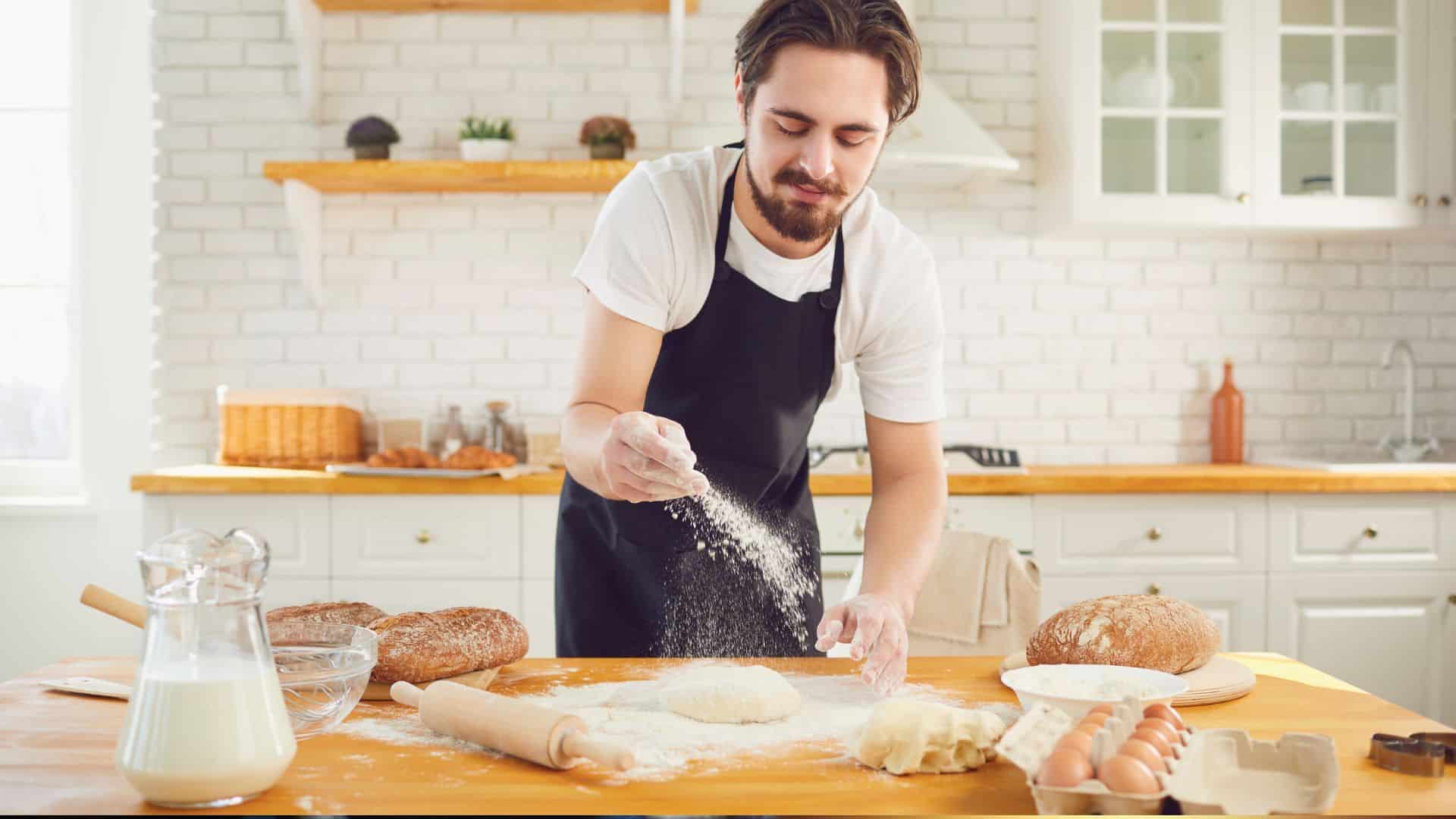 Homme préparant du pain dans une cuisine lumineuse.
