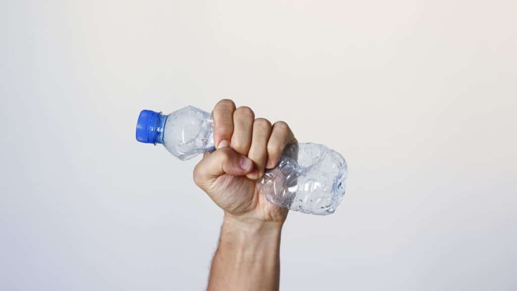 Main serrant une bouteille en plastique écrasée.