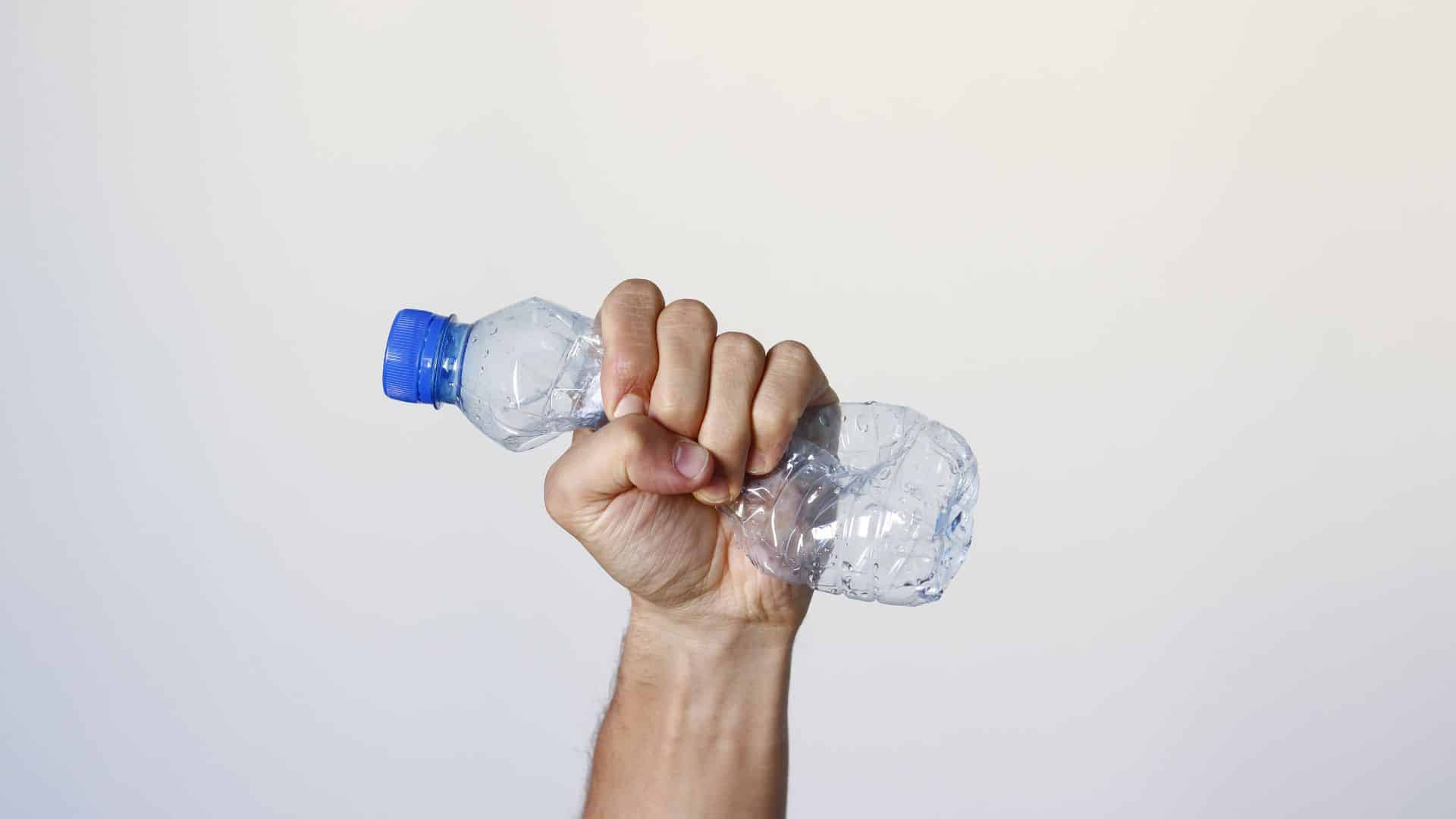 Main serrant une bouteille en plastique écrasée.