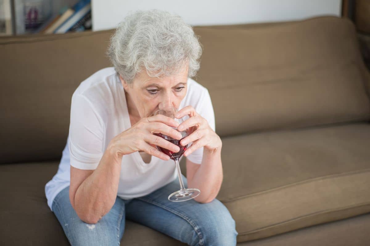 Personne âgée buvant du vin sur un canapé.