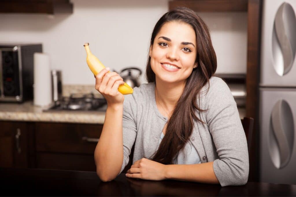 Femme souriante tenant une banane dans la cuisine.