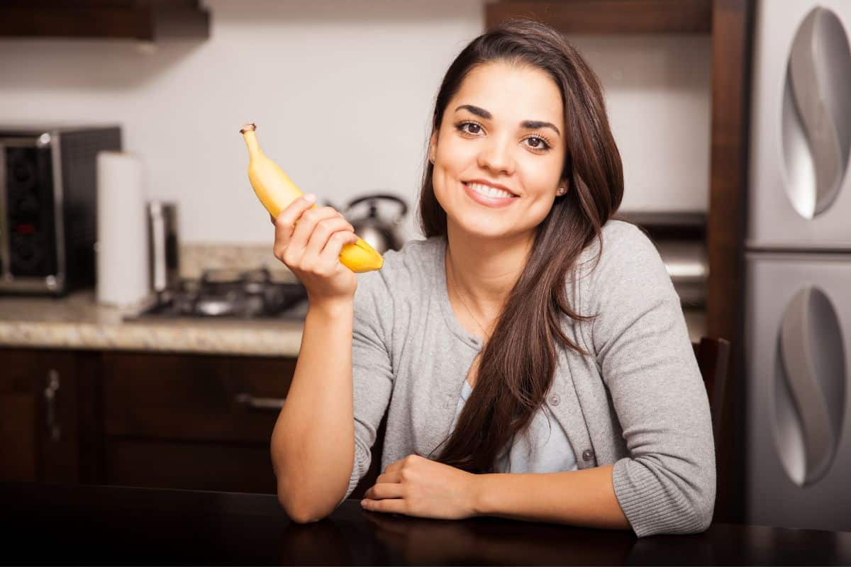 Femme souriante tenant une banane dans la cuisine.