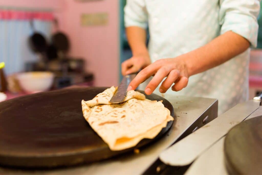 Personne préparant une crêpe sur une plaque chauffante.