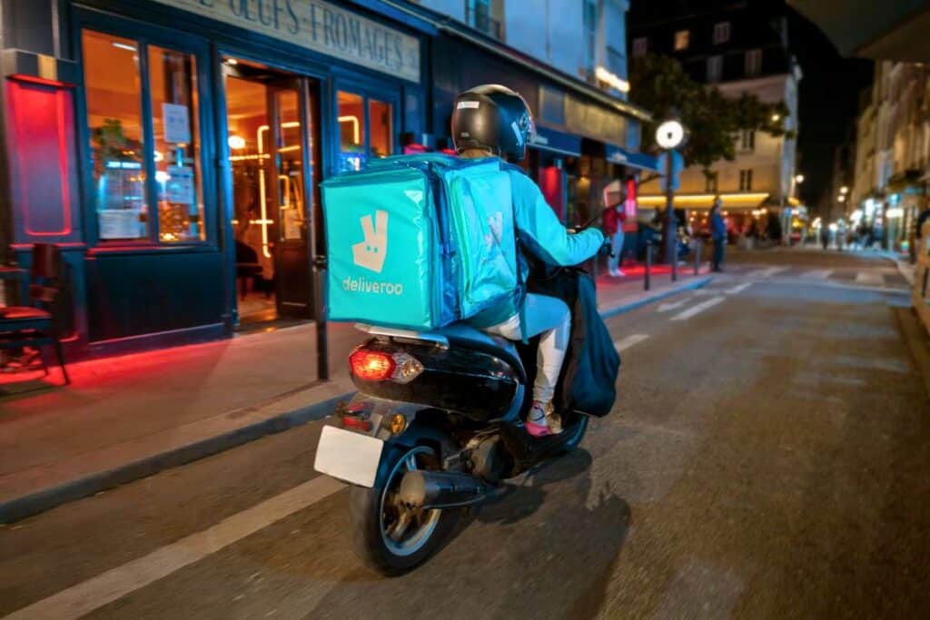 Livreur Deliveroo en scooter dans une rue parisienne.