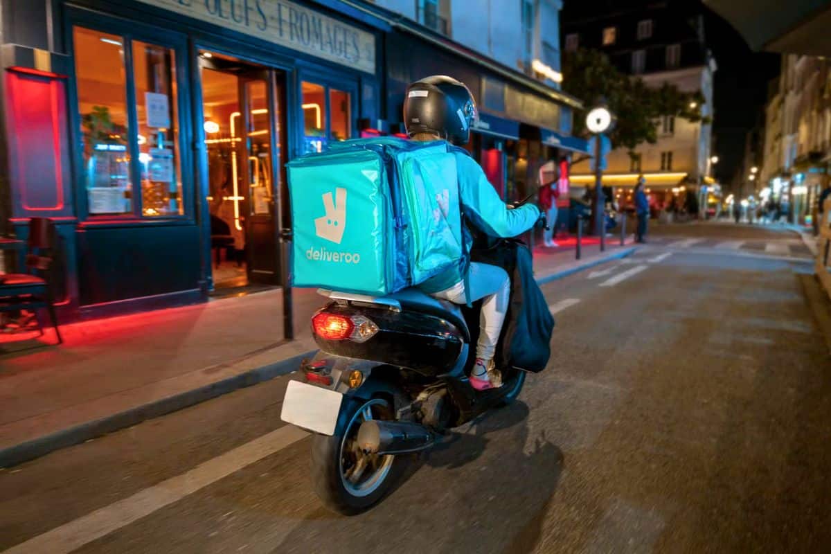 Livreur Deliveroo en scooter dans une rue parisienne.