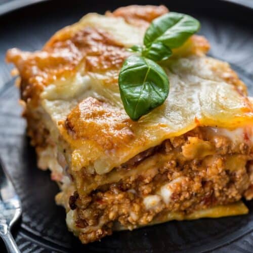 Lasagne bolognaise avec basilic sur assiette noire.