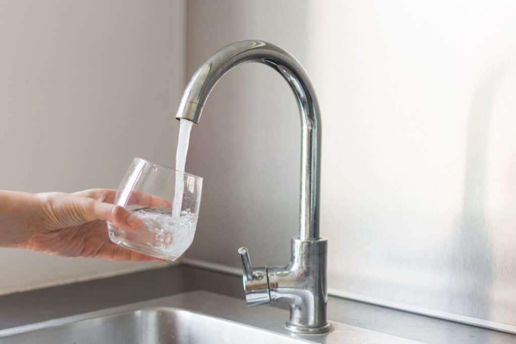 Main remplissant un verre à un robinet.