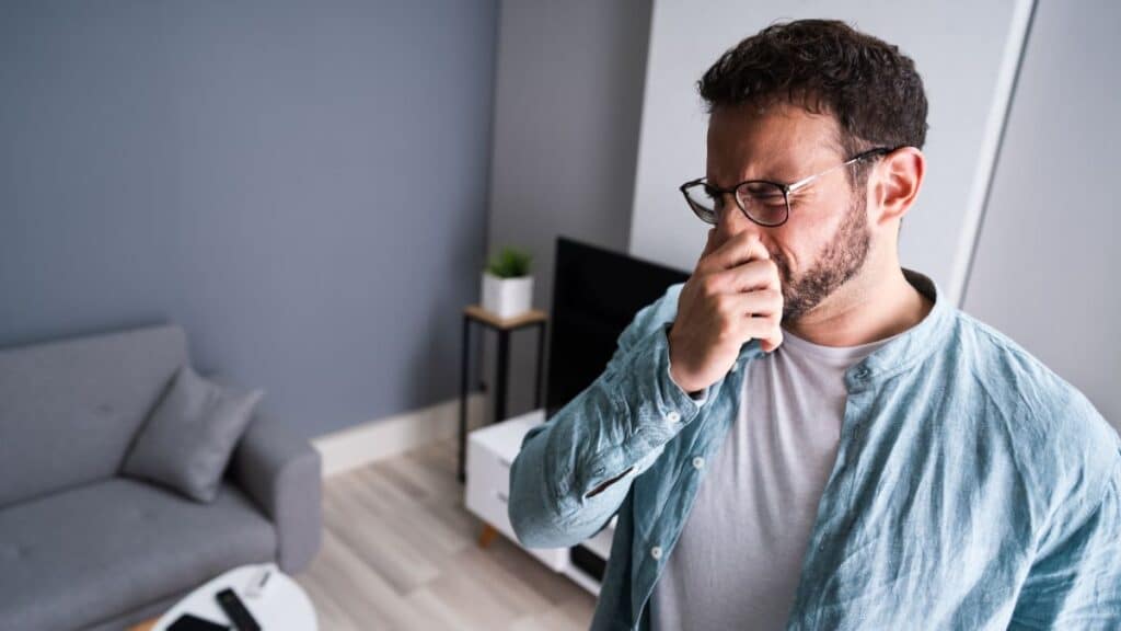 Homme se bouchant le nez dans un salon.