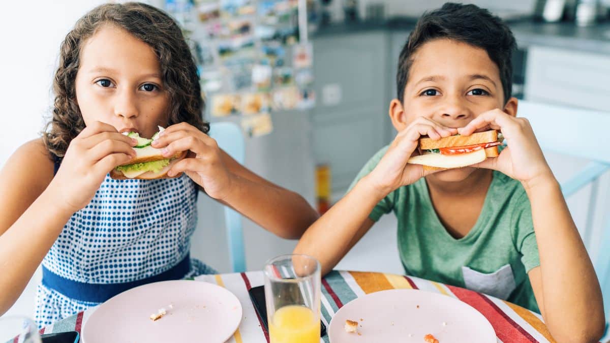 Enfants mangeant des sandwiches à table.