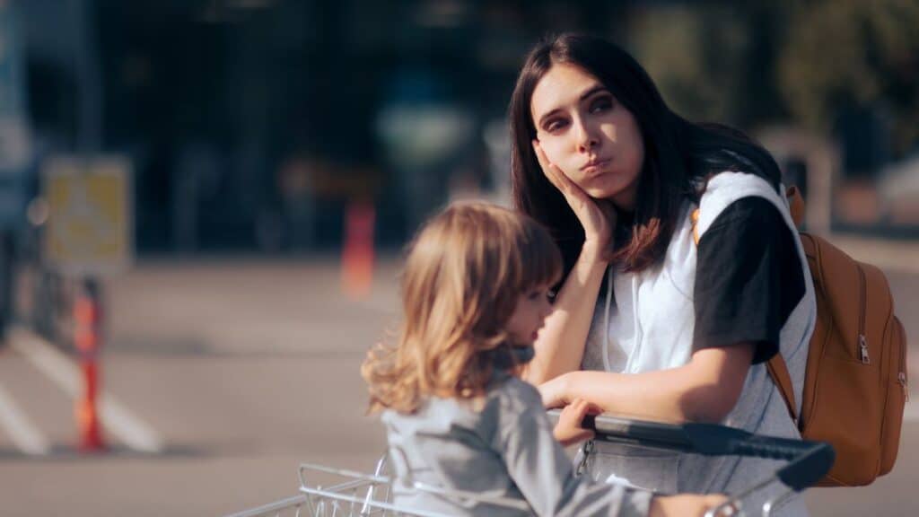 Femme pensive avec enfant près d'un caddie.