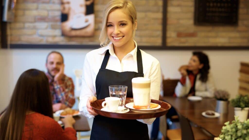 Serveuse souriante portant un plateau dans un café.