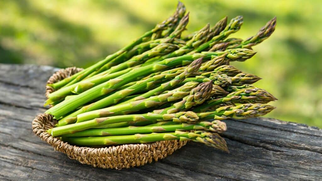 Panier d'asperges vertes sur table en bois.
