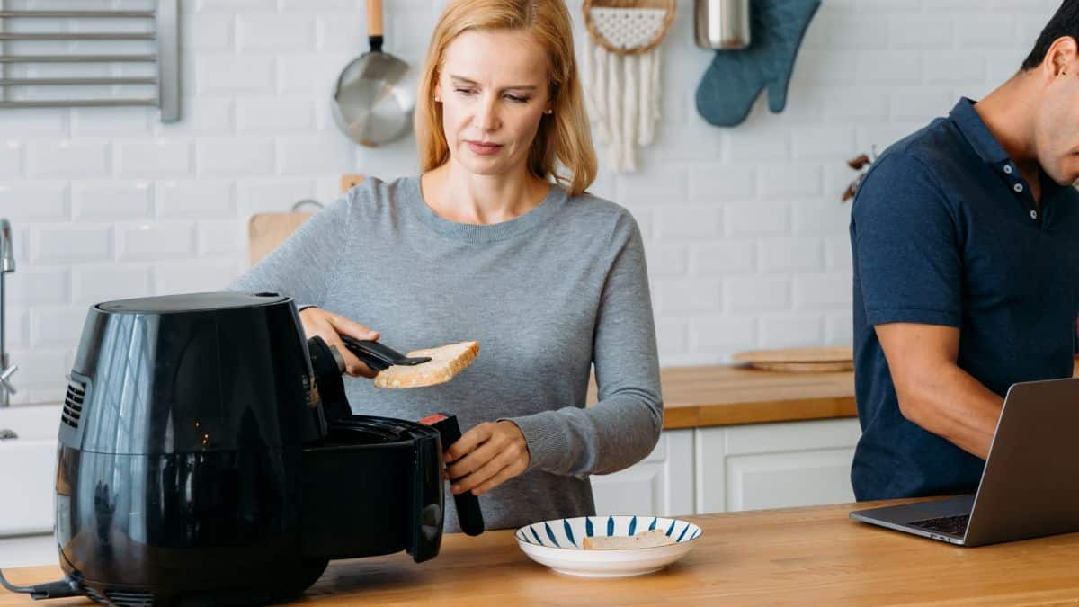 Personne utilisant une friteuse à air dans la cuisine.