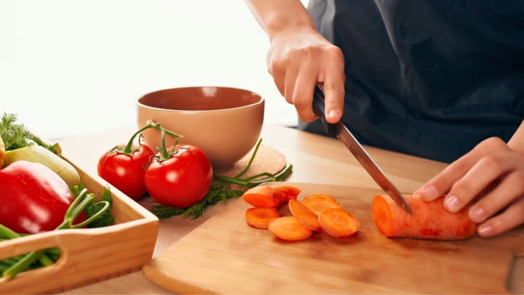 Personne coupant des carottes sur planche à découper.