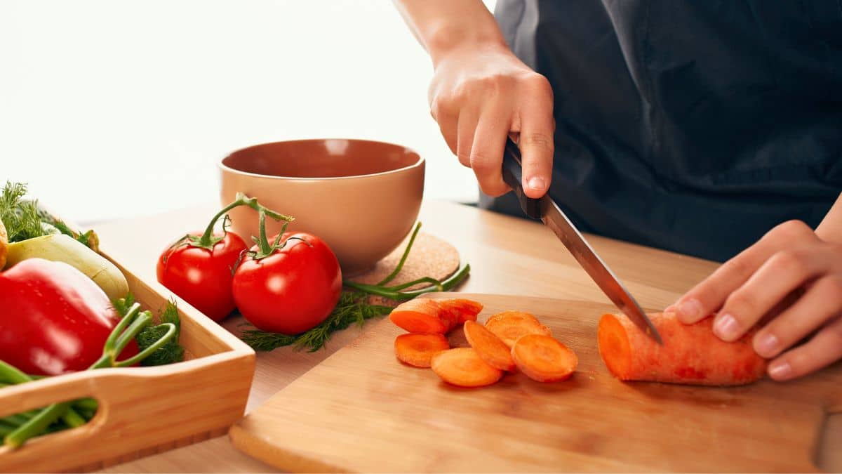 Personne coupant des carottes sur planche à découper.