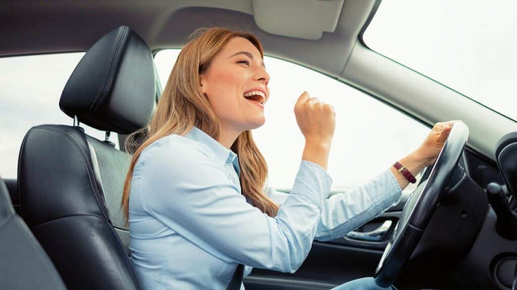 Femme souriante chantant au volant d'une voiture.