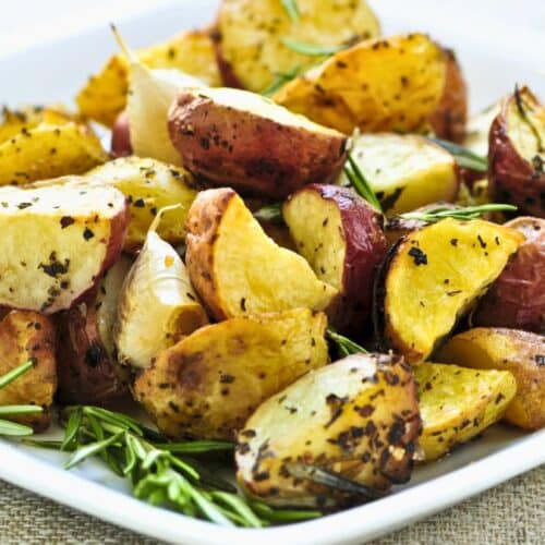Pommes de terre rôties avec herbes sur assiette blanche.