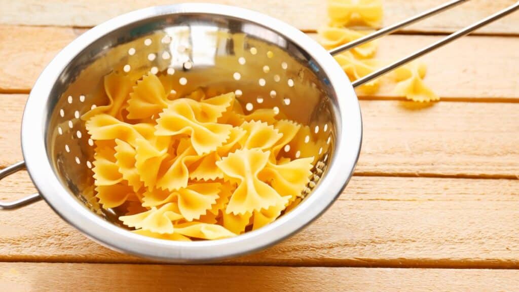 Farfalle crues dans une passoire sur table en bois.