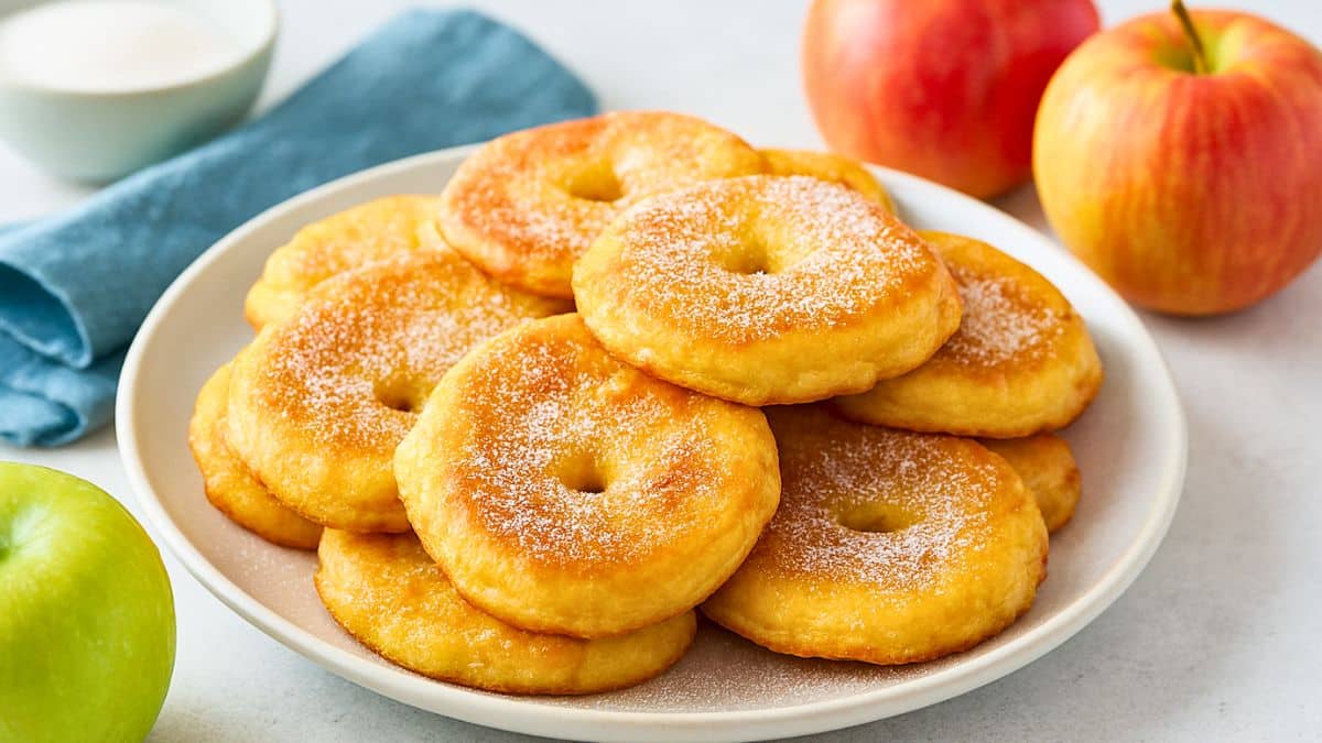 Beignets de pommes saupoudrés de sucre sur assiette blanche.