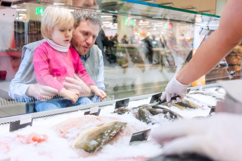 Homme et enfant choisissent poissons chez le poissonnier.