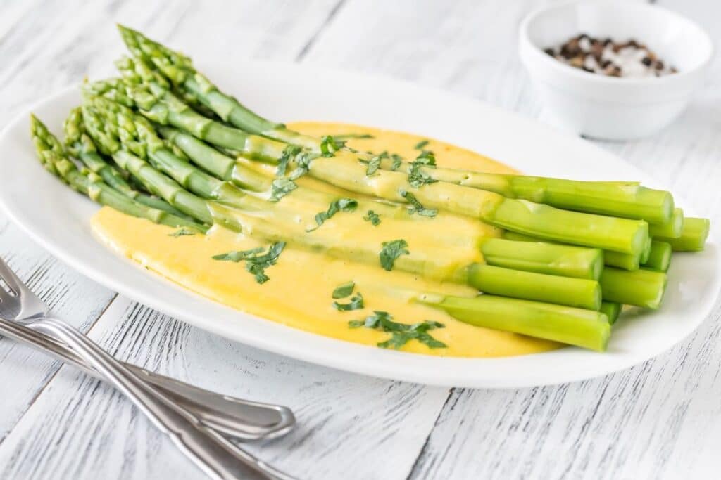 Asperges avec sauce hollandaise sur assiette blanche.