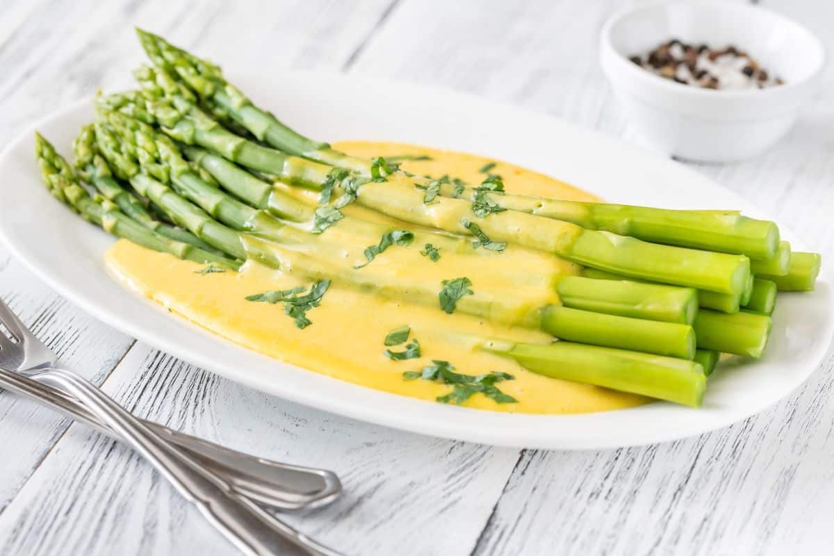 Asperges avec sauce hollandaise sur assiette blanche.