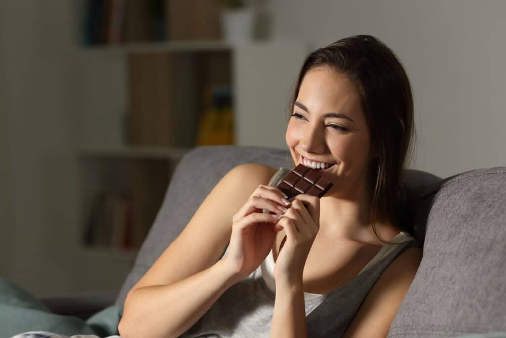 Femme souriante mangeant du chocolat sur canapé.