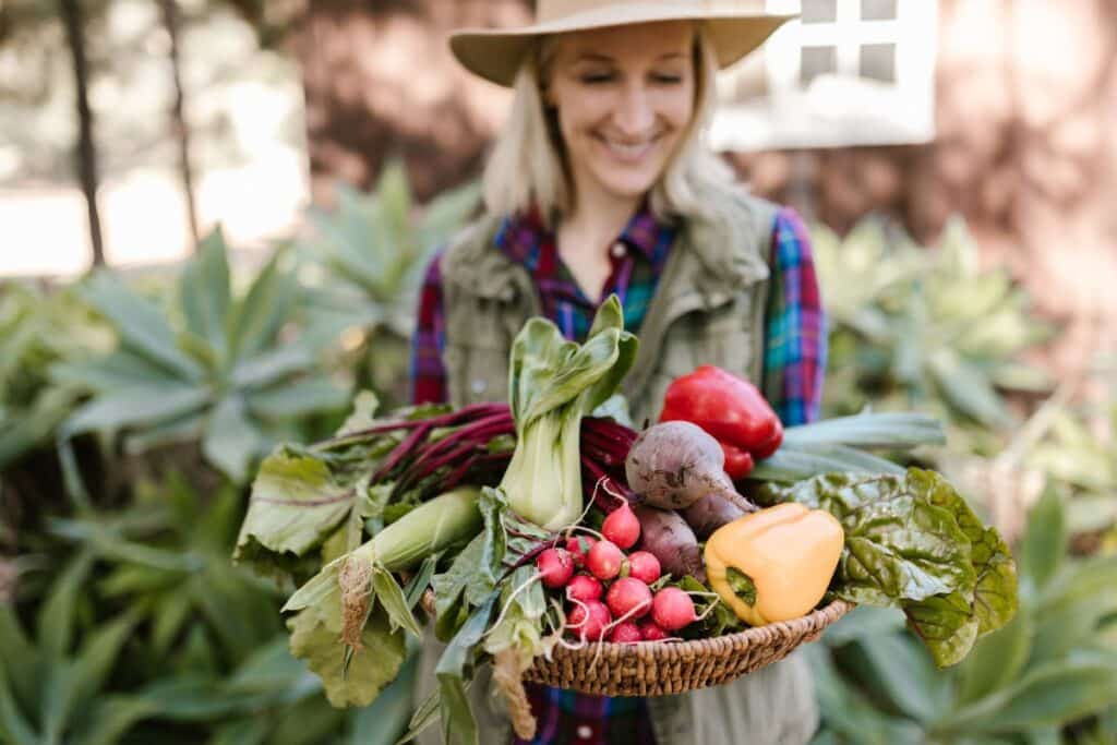Femme souriante tenant légumes frais du jardin.