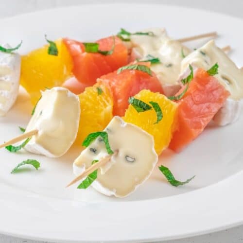 Brochettes fruits fromages sur assiette blanche.