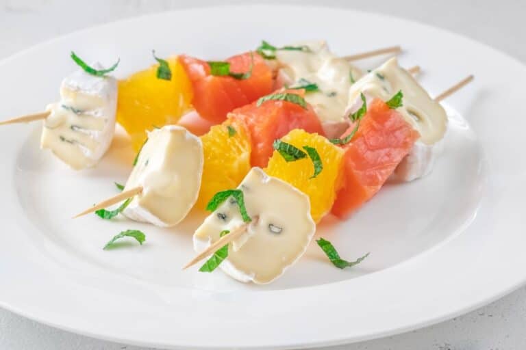 Brochettes fruits fromages sur assiette blanche.
