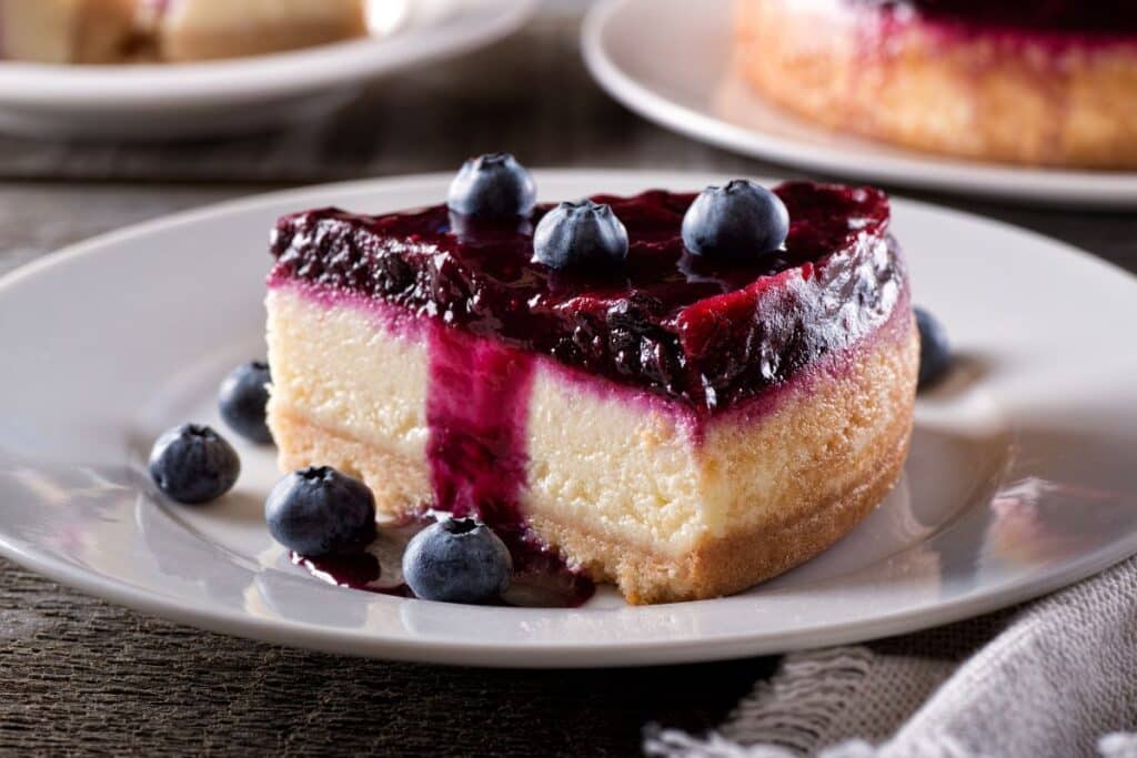 Cheesecake aux myrtilles sur assiette blanche.