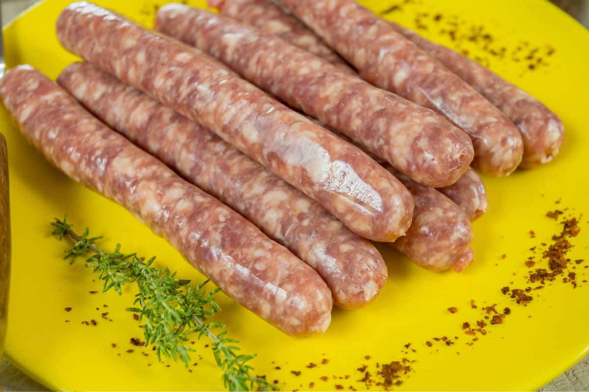 Saucisses crues sur assiette jaune avec herbes