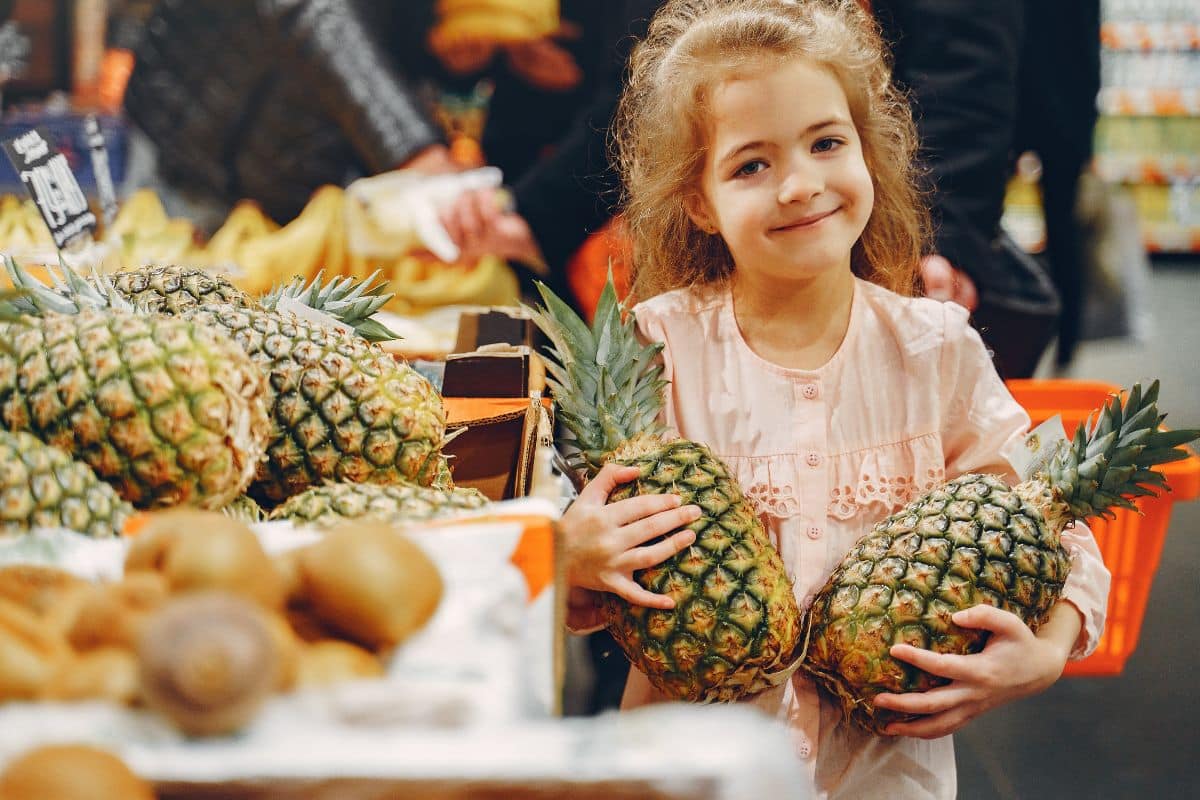 Enfant souriante tenant deux ananas au marché.