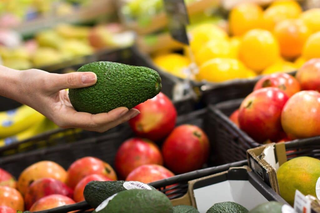 Personne tenant un avocat dans un marché de fruits.