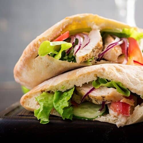 Sandwich pita poulet crudités sur planche bois.