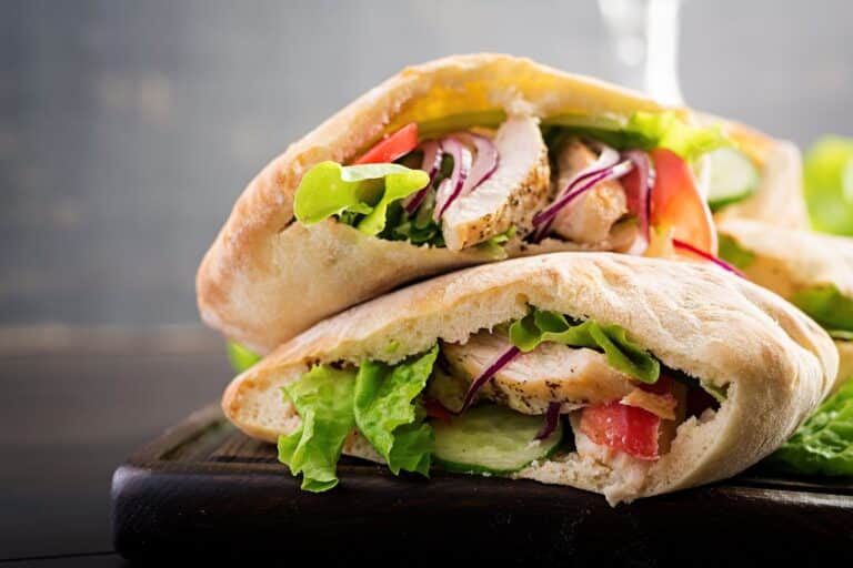Sandwich pita poulet crudités sur planche bois.