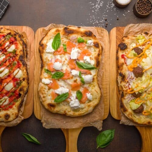 Trois pizzas variées sur planches en bois.