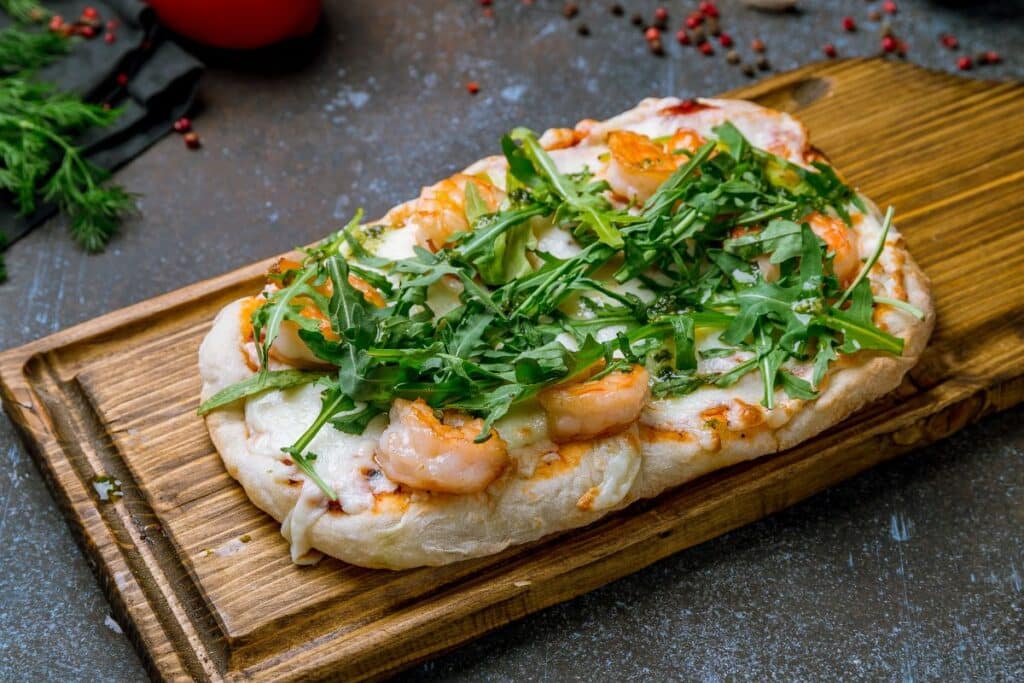 Pizza aux crevettes et roquette sur planche.