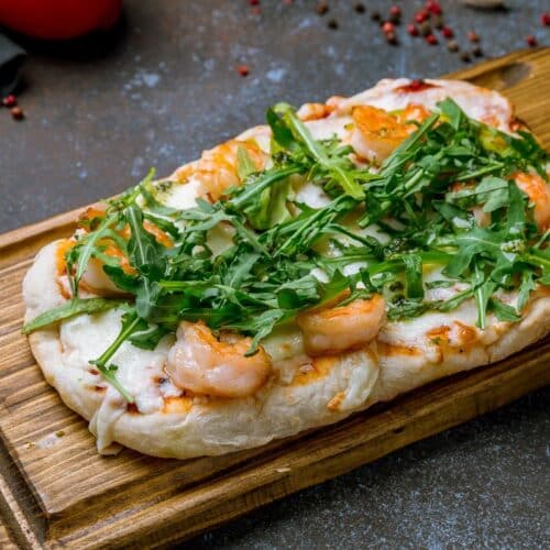 Pizza aux crevettes et roquette sur planche.