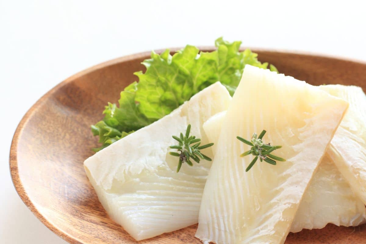 Filets de poisson avec salade sur assiette bois.