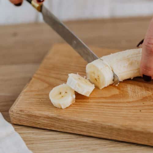 Personne coupant une banane sur une planche.