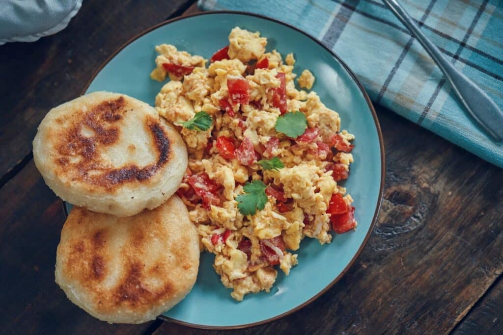 Assiette de brouillade d'œufs aux légumes et arepas.