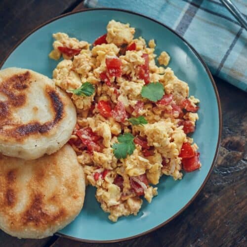 Assiette de brouillade d'œufs aux légumes et arepas.